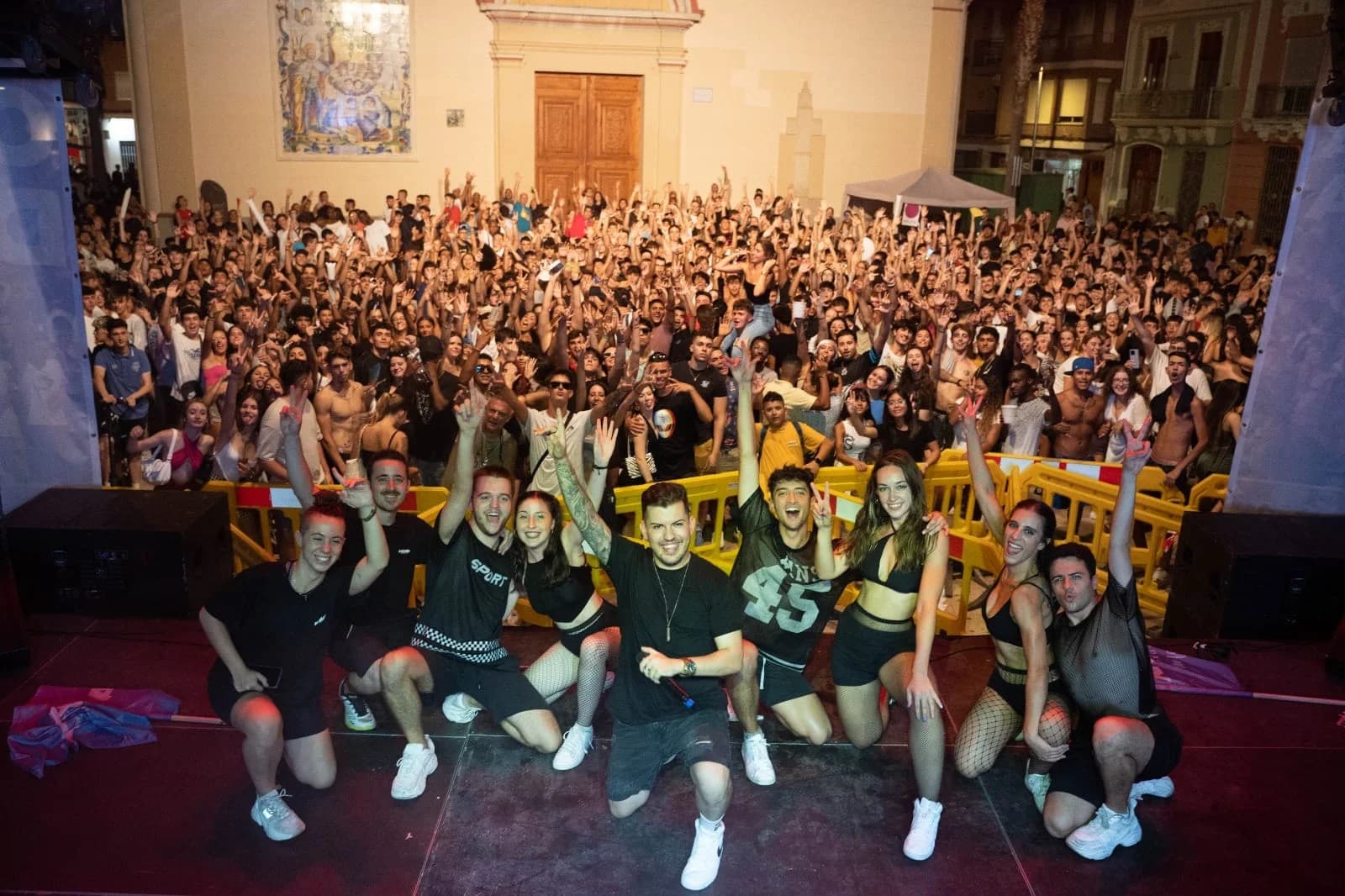 El equipo de CULTUCREA en el escenario, de noche, con la plaza llena de público con las manos en alto