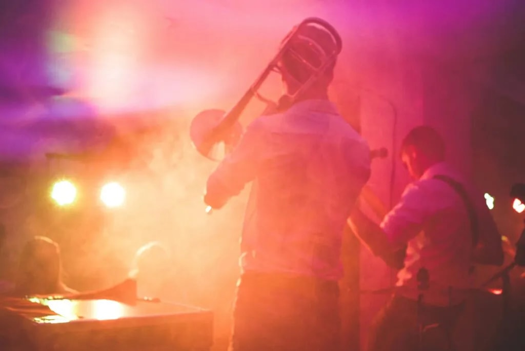 Un trombonista y un guitarrista tocando en directo entre luces de colores y humo