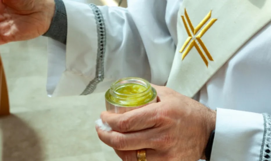 Las manos de un sacerdote sosteniendo el óleo durante una confirmación