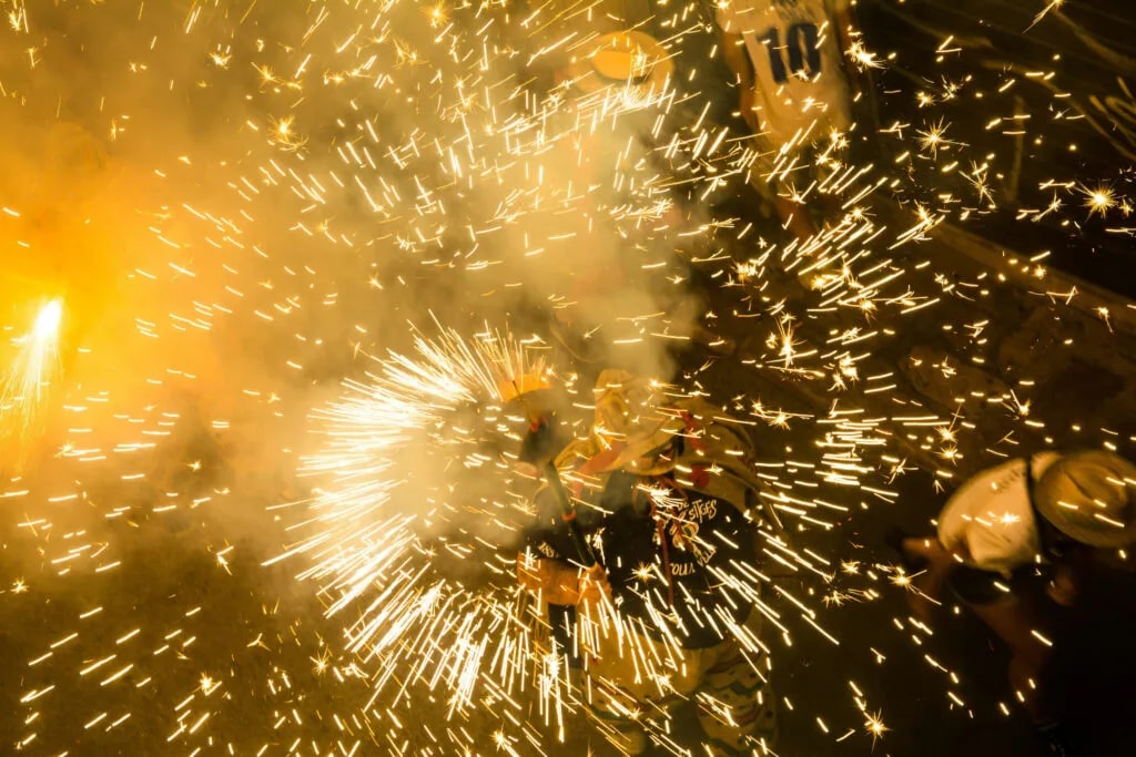 Una figura encapuchada rodeada de chispas de pirotecnia durante un correfoc nocturno