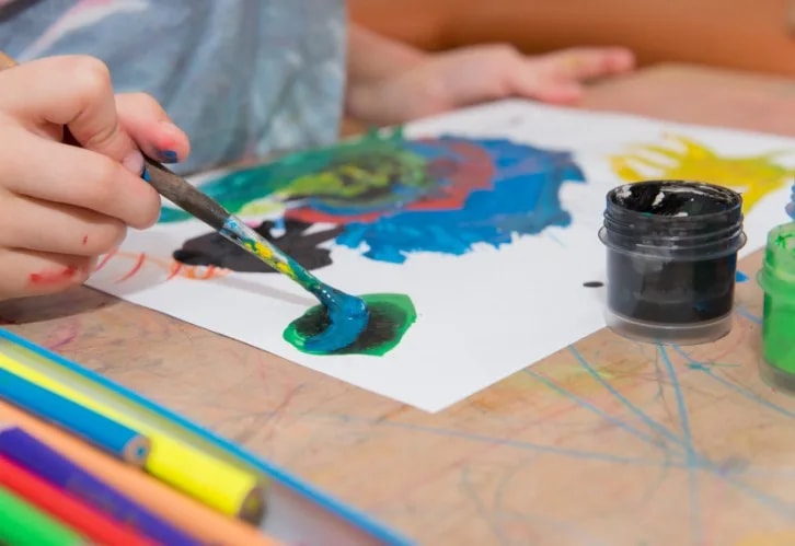 Manos de una niña pintando con témperas sobre una cartulina en un taller creativo