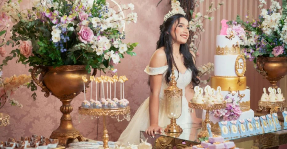 Una joven junto a la mesa dulce de su celebración, entre flores y tartas