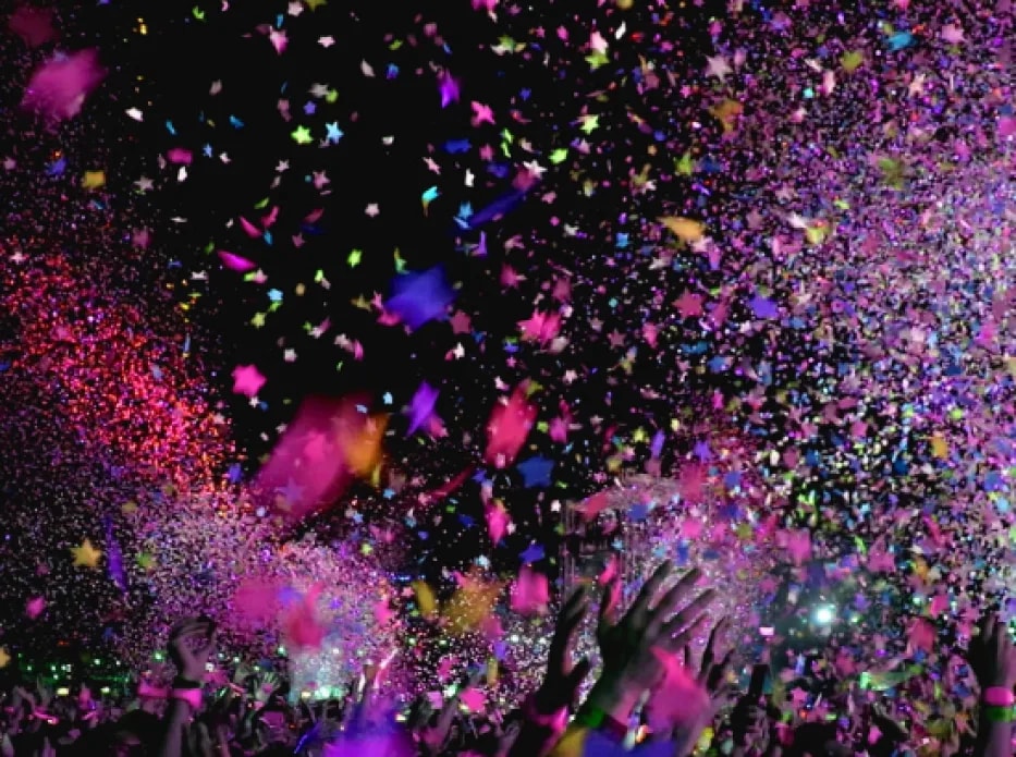 Explosión de confeti de colores sobre el público con las manos en alto, de noche