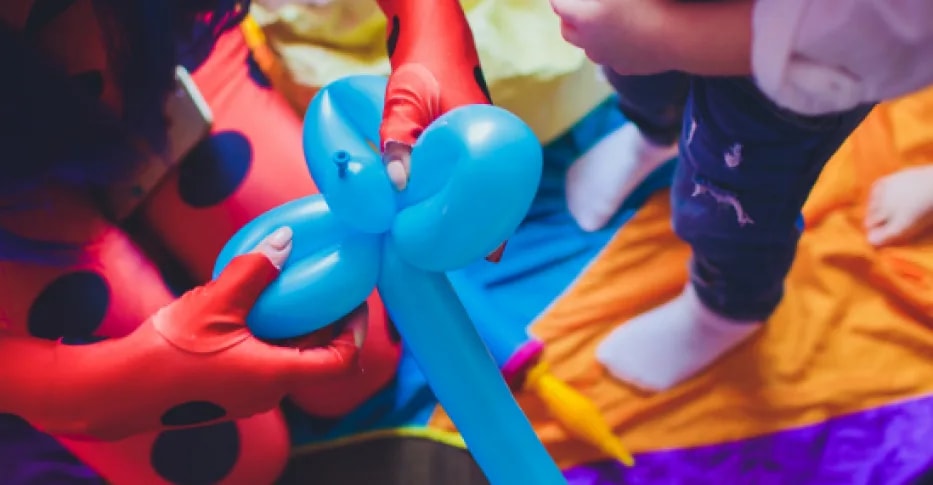 Figuras de globoflexia —una mariquita y un perro— en el suelo, entre los pies de los niños que juegan