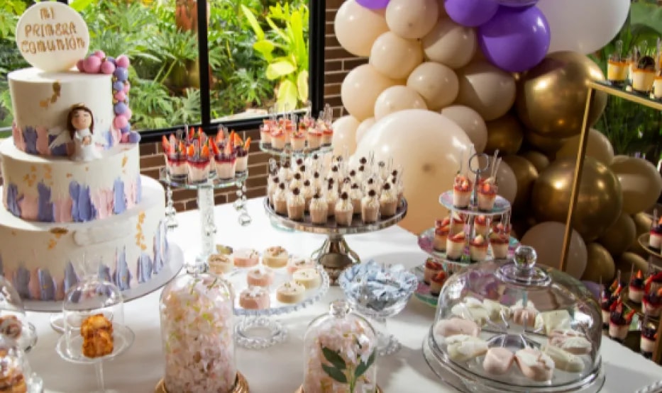 Tarta de primera comunión y mesa dulce decorada con globos y flores