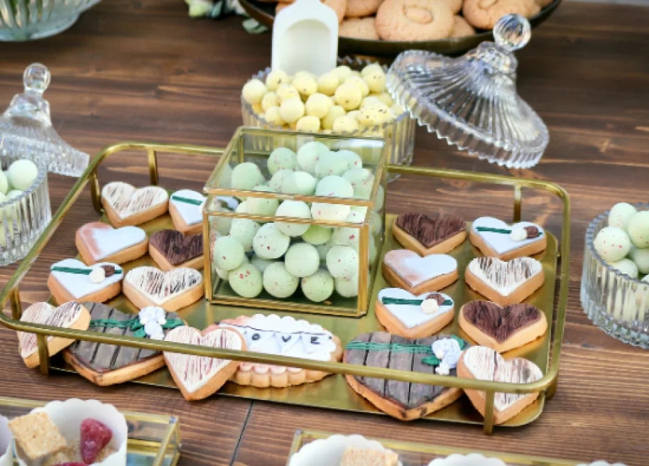 Mesa dulce con galletas decoradas y bandejas de dulces sobre soportes dorados