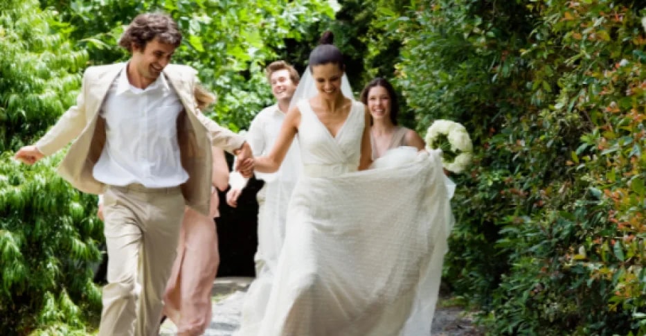 Los novios corriendo por el jardín, de la mano y rodeados de sus invitados